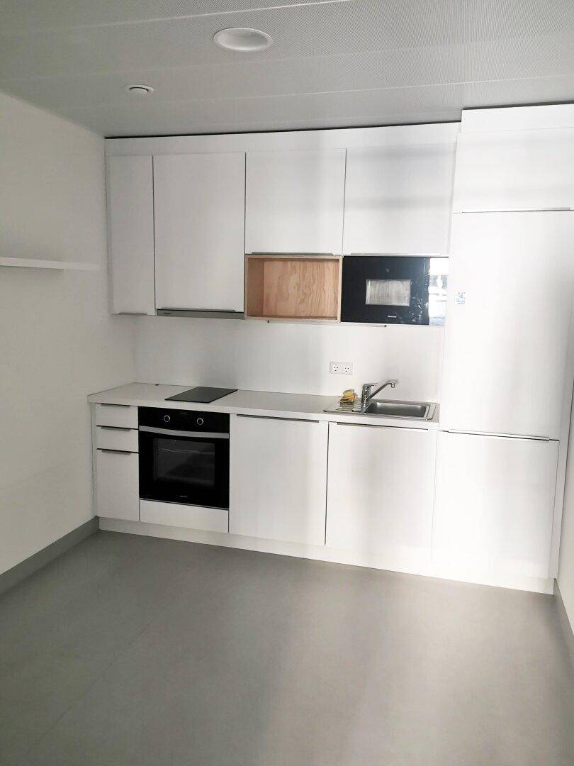 Moderne Küchenzeile mit weißen Schränken, integriertem Backofen und Induktionskochfeld.