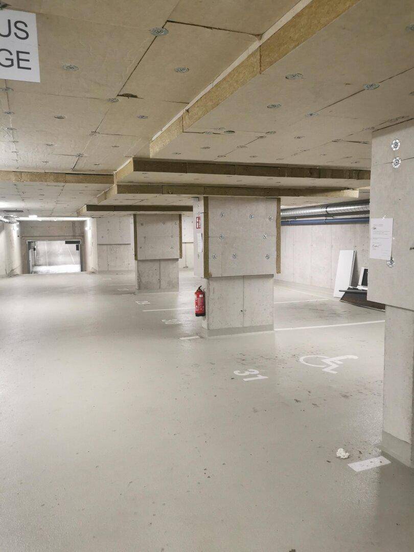 Tiefgarage mit Betonpfeilern und markierten Stellplätzen, inklusive Behindertenparkplatz.