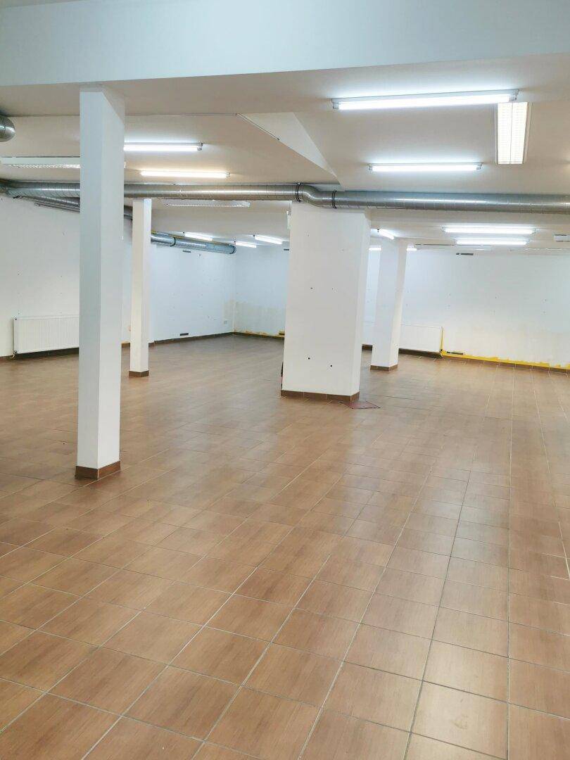 Großer, offener Geschäftsraum mit Stützpfeilern, Fliesenboden und sichtbaren Lüftungsleitungen an der Decke.