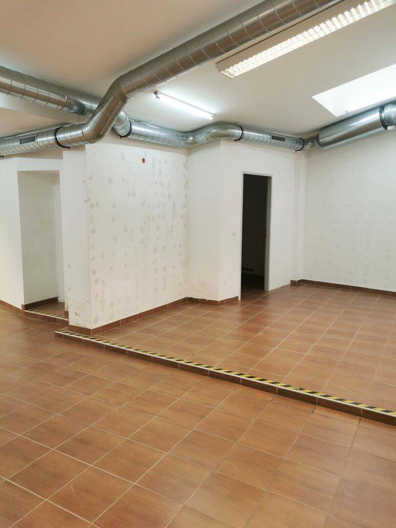 Innenansicht des Ladenlokals mit sichtbaren Lüftungsrohren und braunen Fliesen auf dem Boden.