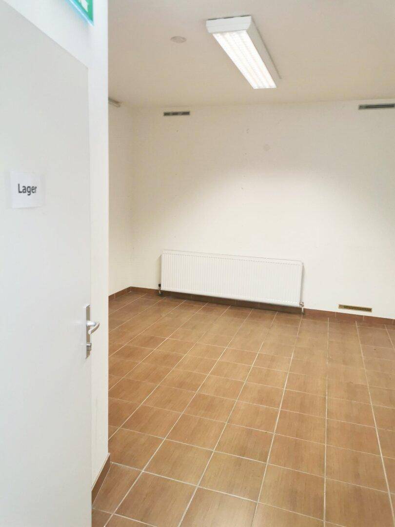 Kleiner Lagerraum mit Fliesenboden, weißen Wänden und einem Heizkörper unter dem Fenster.