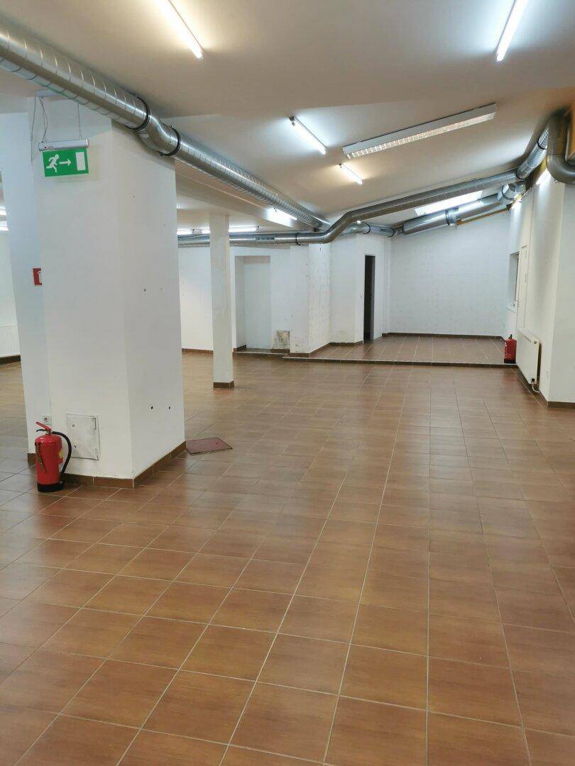 Weitläufiger Geschäftsraum mit Fliesenboden, Säulen und sichtbaren Lüftungsrohren unter der Decke.