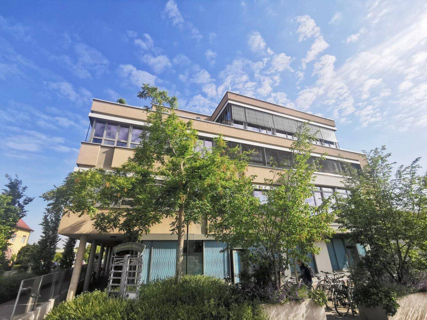 Weitläufige Außenansicht des modernen Bürogebäudes mit viel Grün und klarem Himmel.