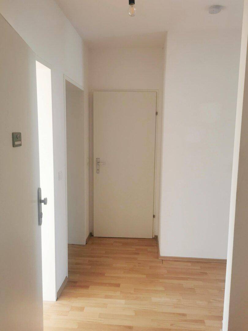 Heller Flur mit Holzboden und weißen Wänden, der zu weiteren Räumen führt.