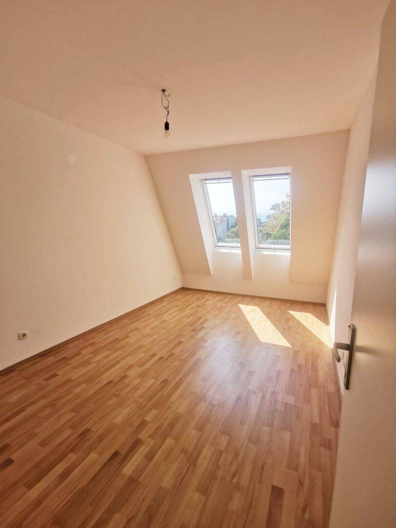 Helles Schlafzimmer mit Holzboden und zwei Dachfenstern, die viel Licht spenden.