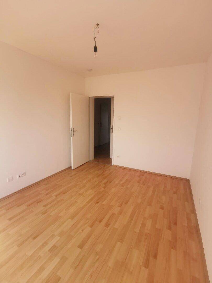 Geräumiges Schlafzimmer mit hellem Holzboden und weißen Wänden, bereit zur Einrichtung.