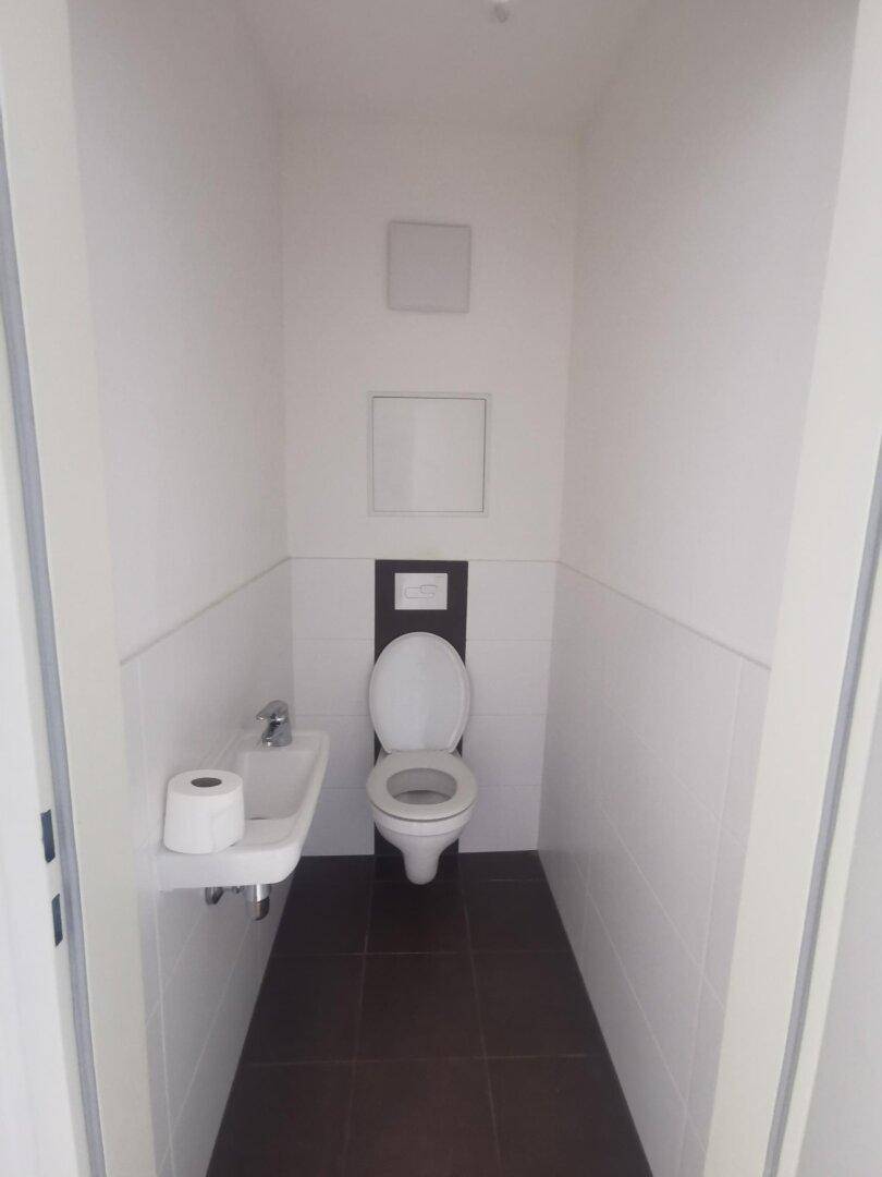 Kleines Gäste-WC mit Wand-WC, Handwaschbecken und zweifarbigen Fliesen.