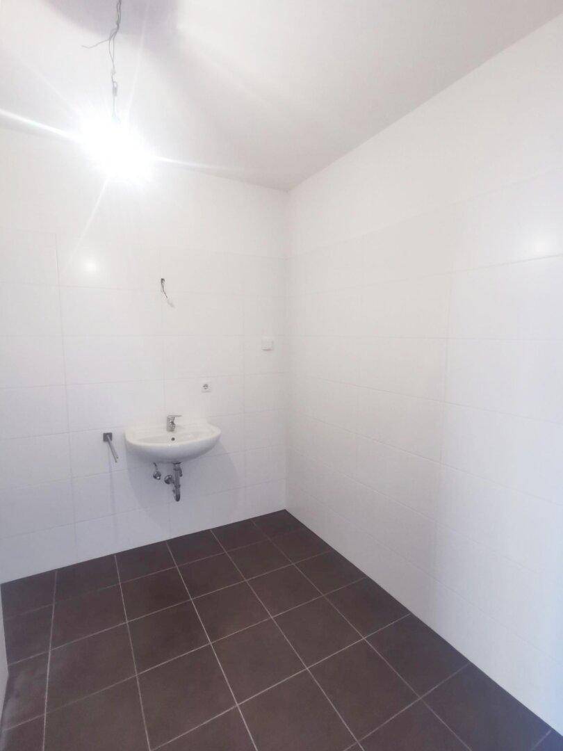 Badezimmer mit weißen Wandfliesen, dunklem Boden und einem einzelnen Waschbecken.