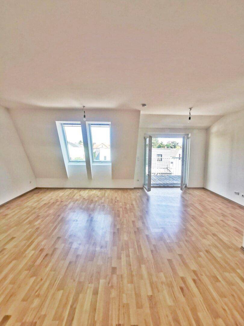 Lichtdurchflutetes Wohnzimmer mit Holzboden, Dachfenstern und Zugang zum Balkon.