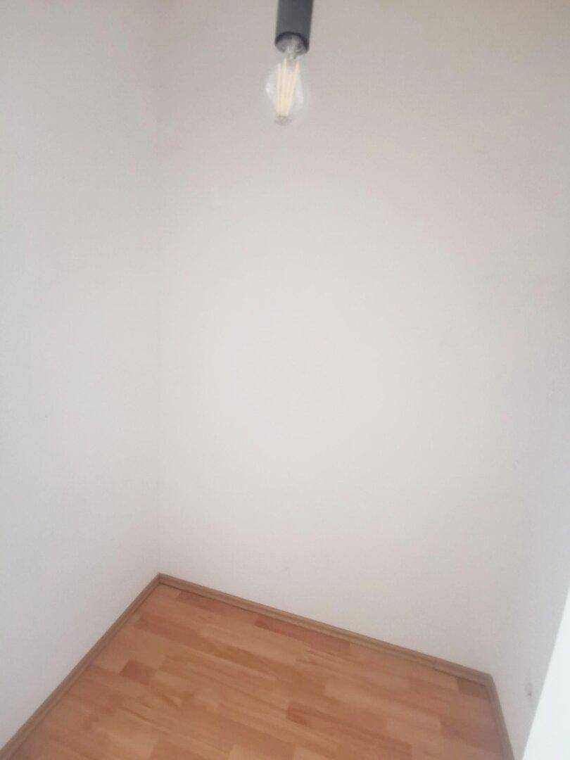 Ecke eines Zimmers mit hellem Holzboden und weißen Wänden, schlicht gehalten.