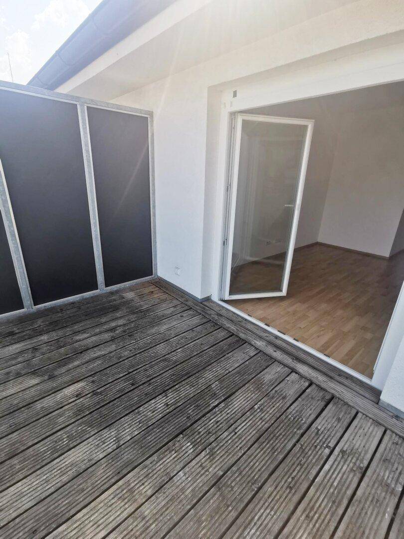 Geräumiger Balkon mit Holzbelag und direktem Zugang zum Innenbereich der Wohnung.