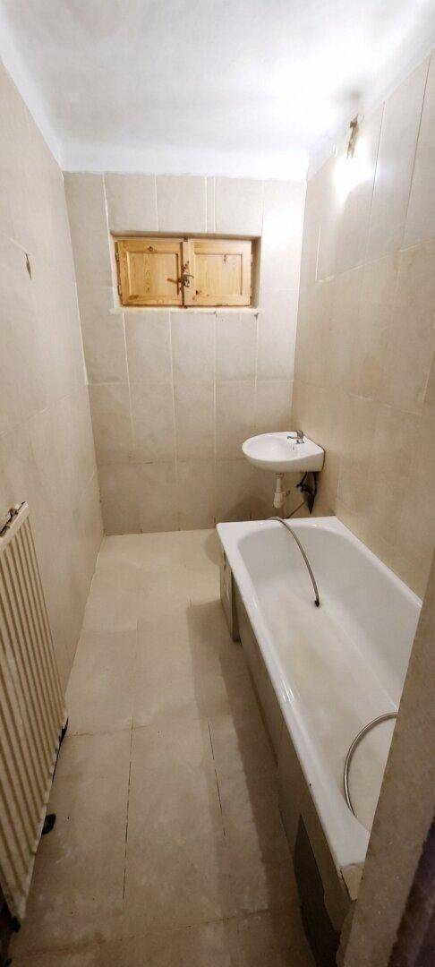 Einfaches Badezimmer mit Badewanne, Waschbecken und einem kleinen Fenster mit Holzläden.