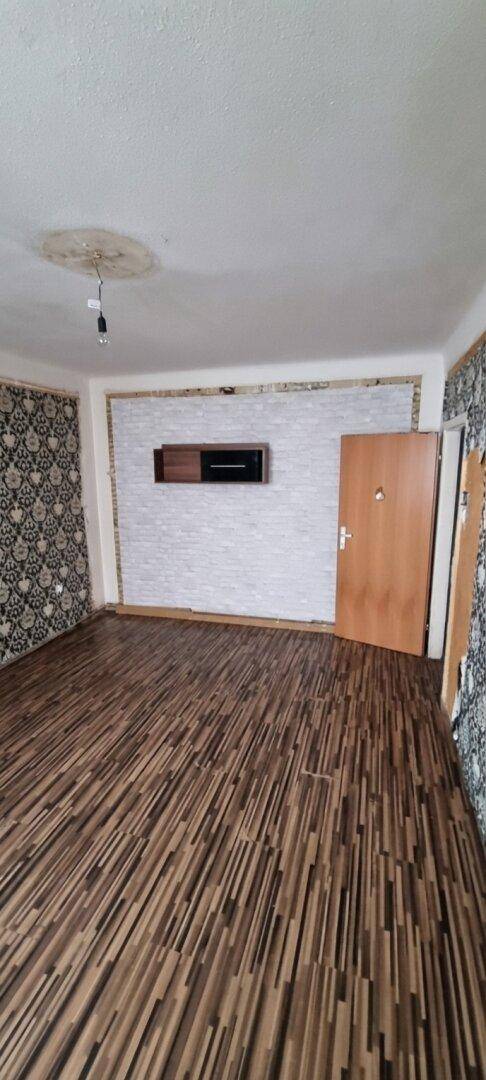 Geräumiger Raum mit Laminatboden, gemusterter Tapete und einer Wanddekoration.