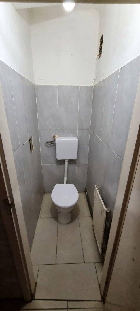 Separate Toilette mit grauen Fliesen an den Wänden und einem kleinen Heizkörper.
