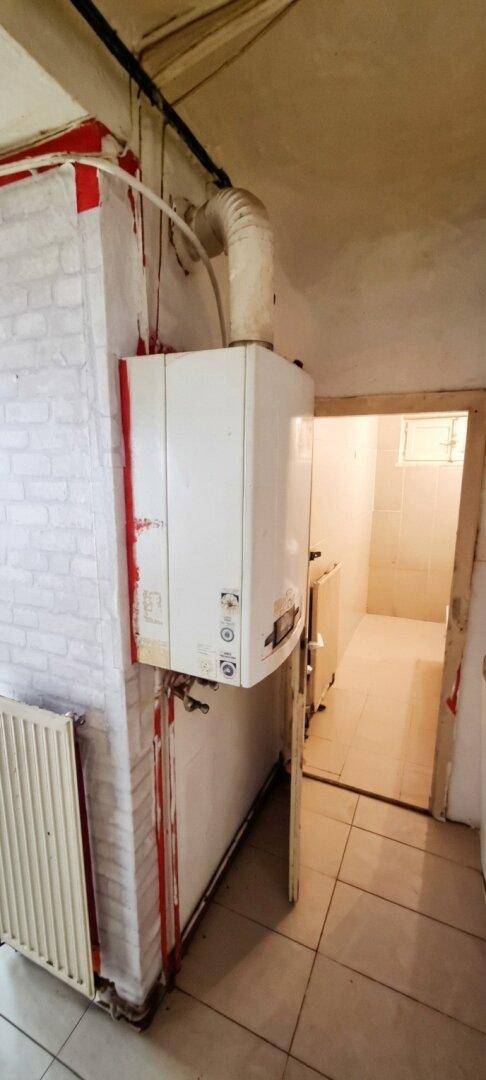 Kleiner Raum mit Gastherme, Heizkörper und Zugang zu einem Badezimmer.