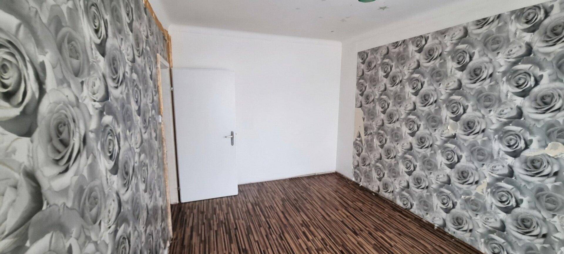 Schlafzimmer mit floraler Tapete, Laminatboden und einer weißen Tür.