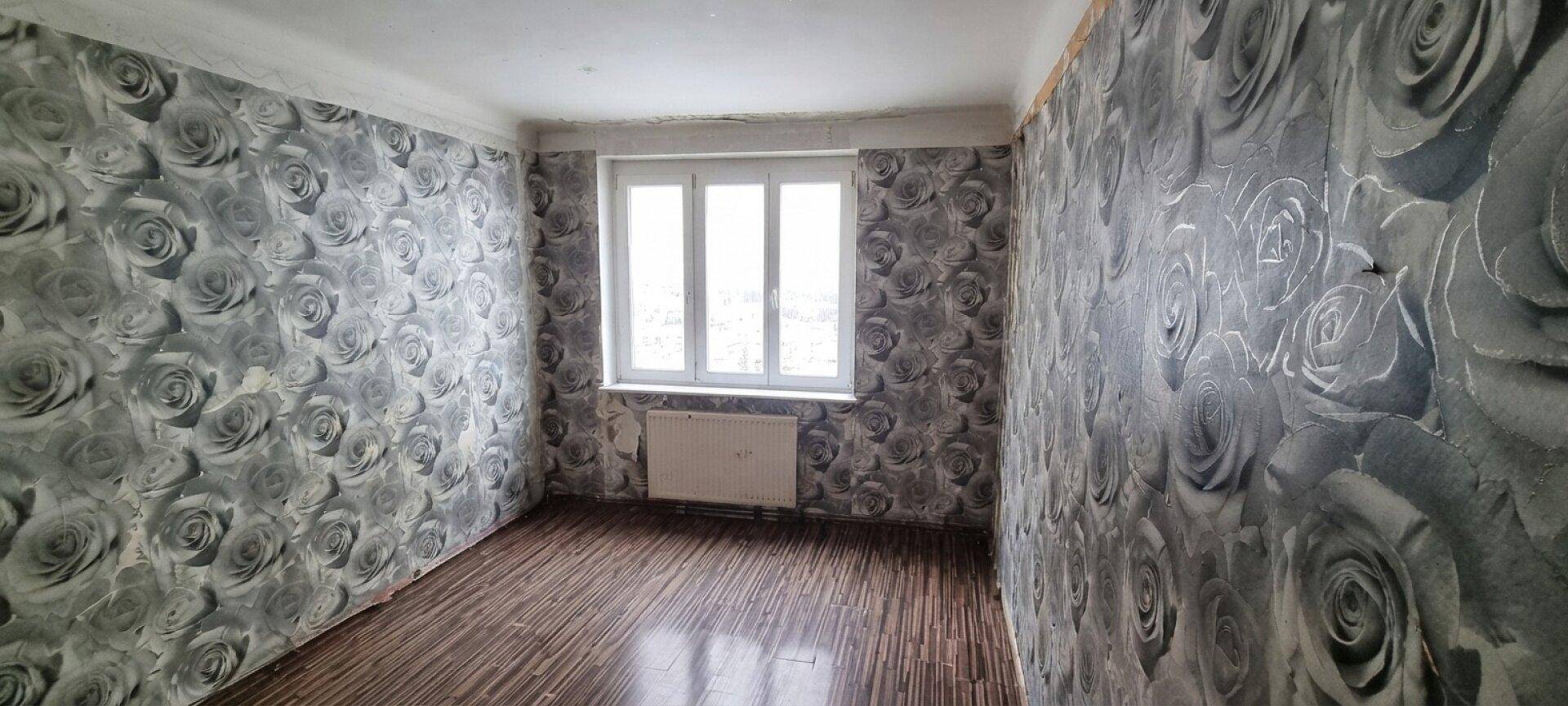 Schlafzimmer mit auffälliger Blumentapete, Laminatboden und einem Fenster.