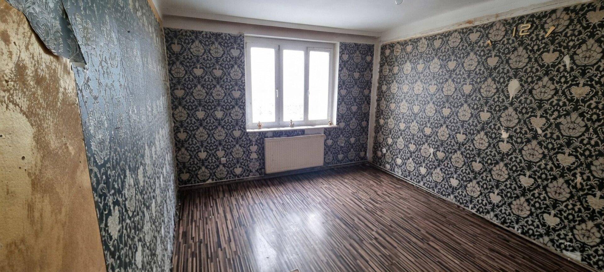 Schlafzimmer mit gemusterter Tapete, Laminatboden und einem großen Fenster.