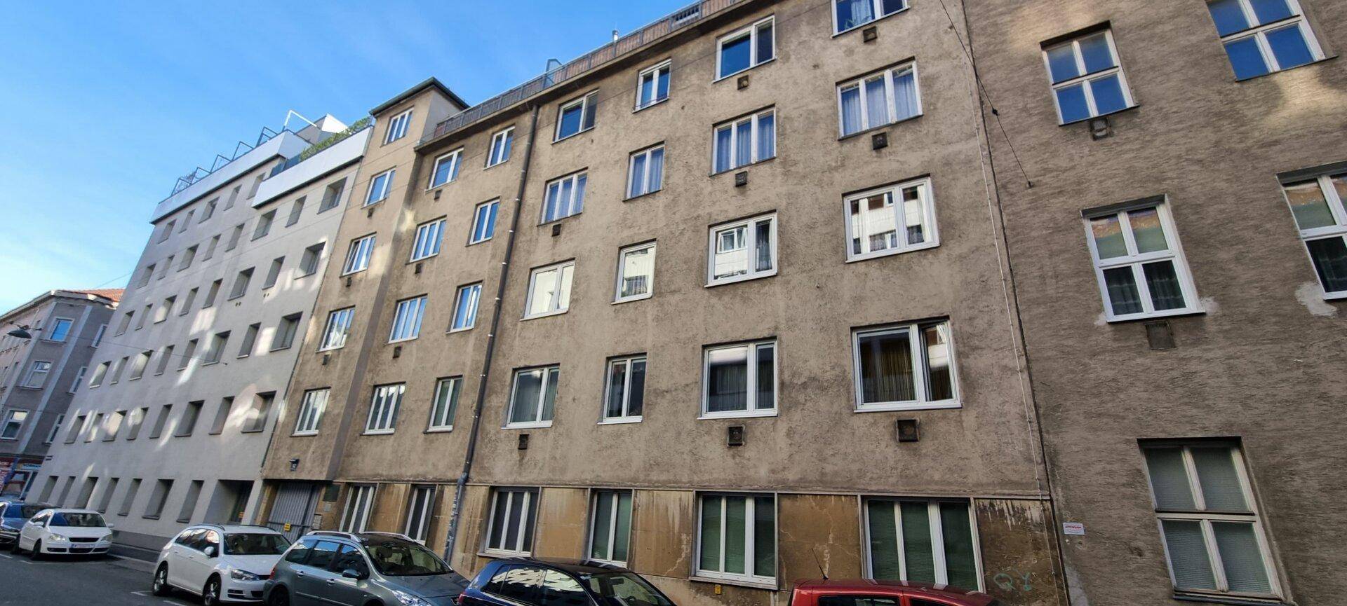 Mehrere Wohngebäude entlang einer Straße mit geparkten Autos unter blauem Himmel.