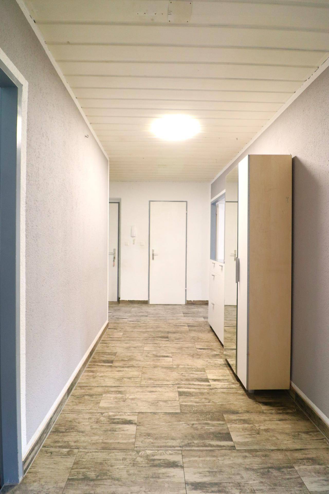 Heller Flur mit Holzoptik-Boden und Spiegelschrank, führt zu weiteren Räumen der Wohnung.