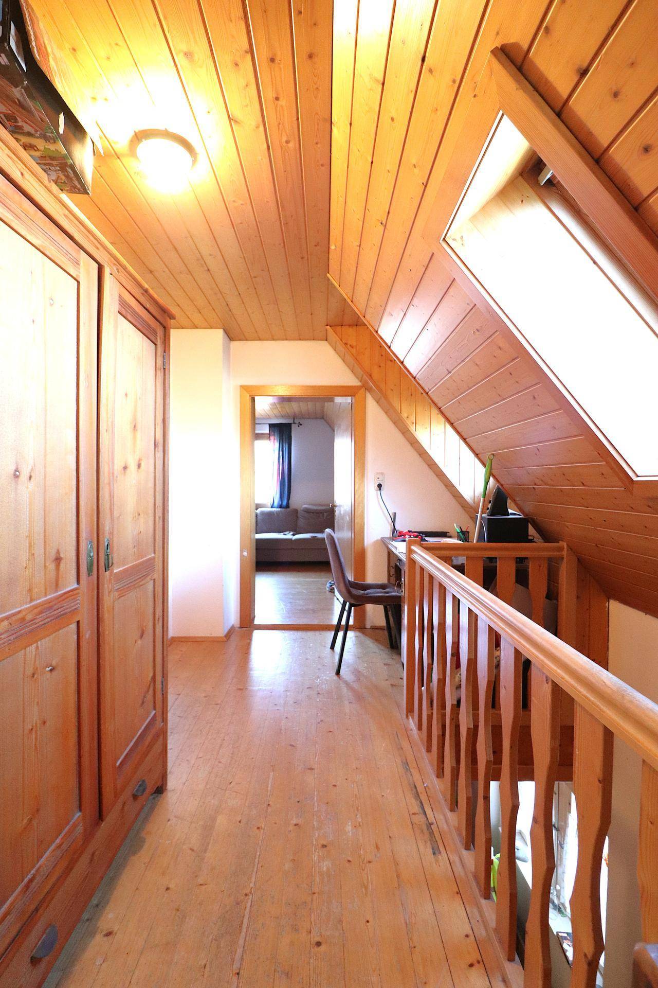 Heller Dachgeschossflur mit Holzvertäfelung, Schreibtisch und Blick in angrenzende Räume.