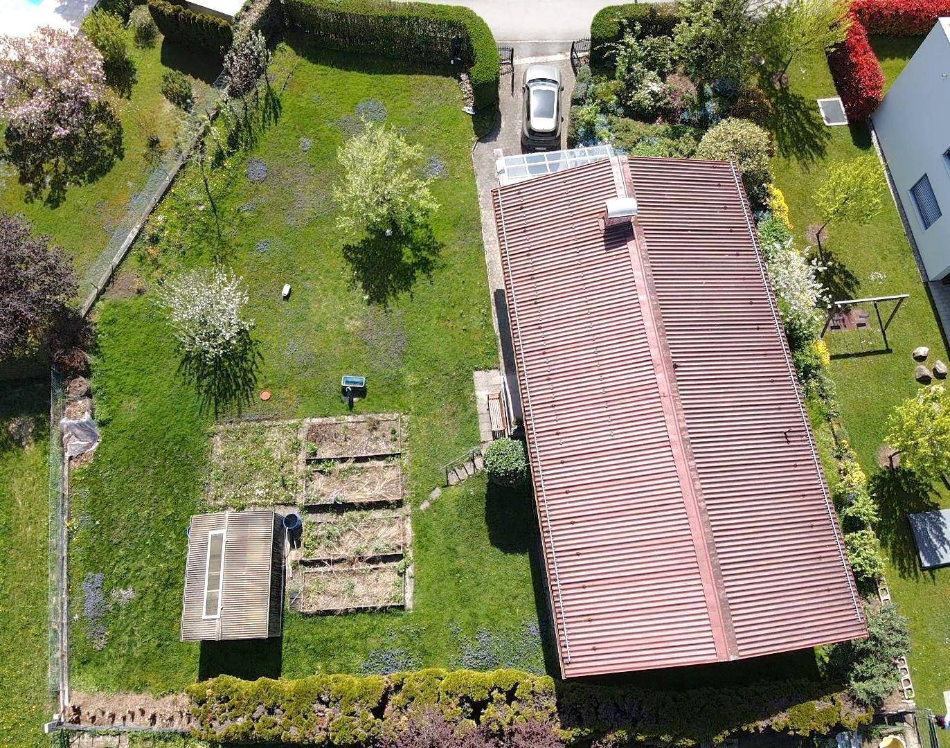 Vogelperspektive des Hauses mit rotem Satteldach, großem Garten und Gewächshaus.