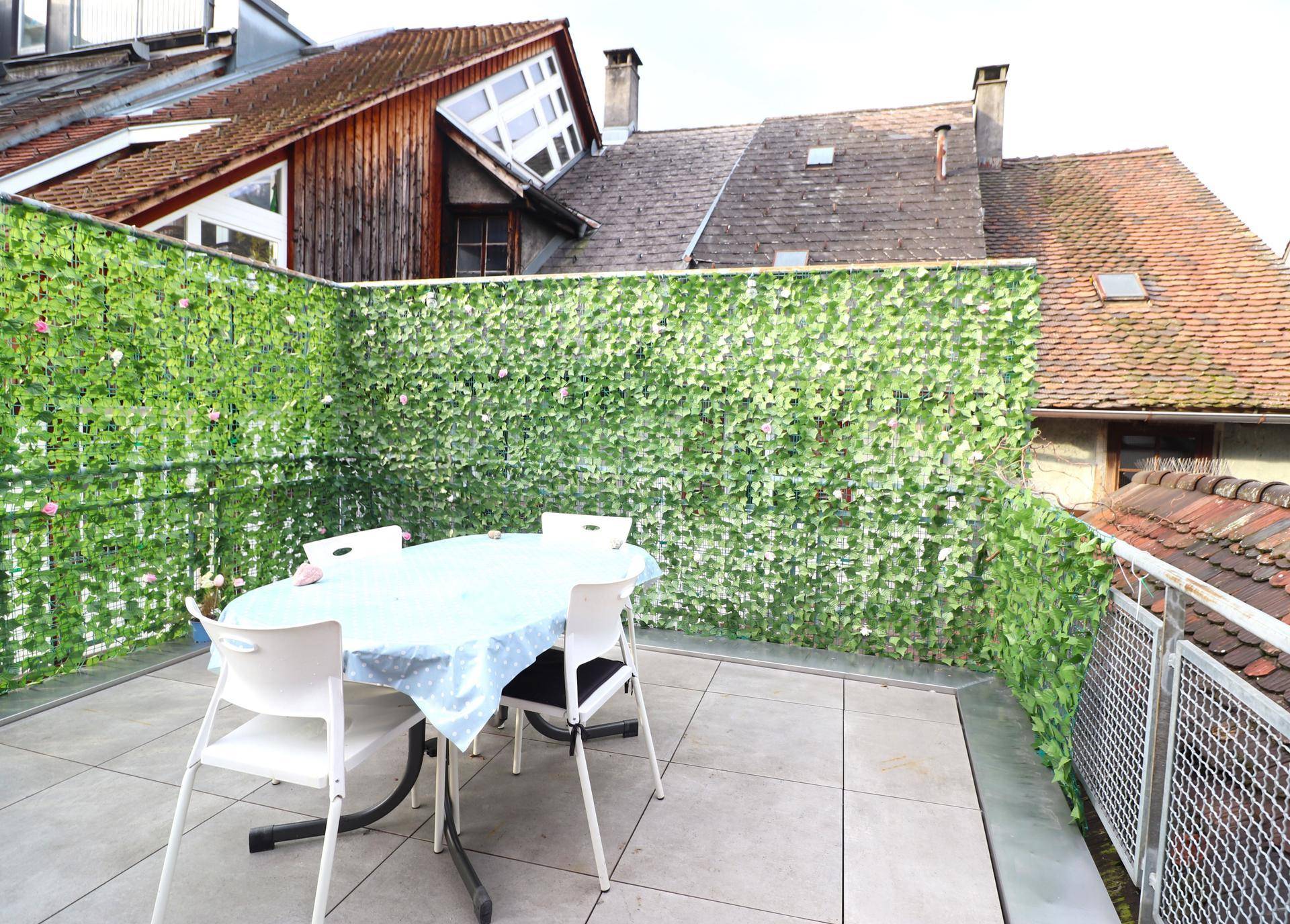 Gemütliche Dachterrasse mit Esstisch und grüner Sichtschutzwand für Privatsphäre im Freien.