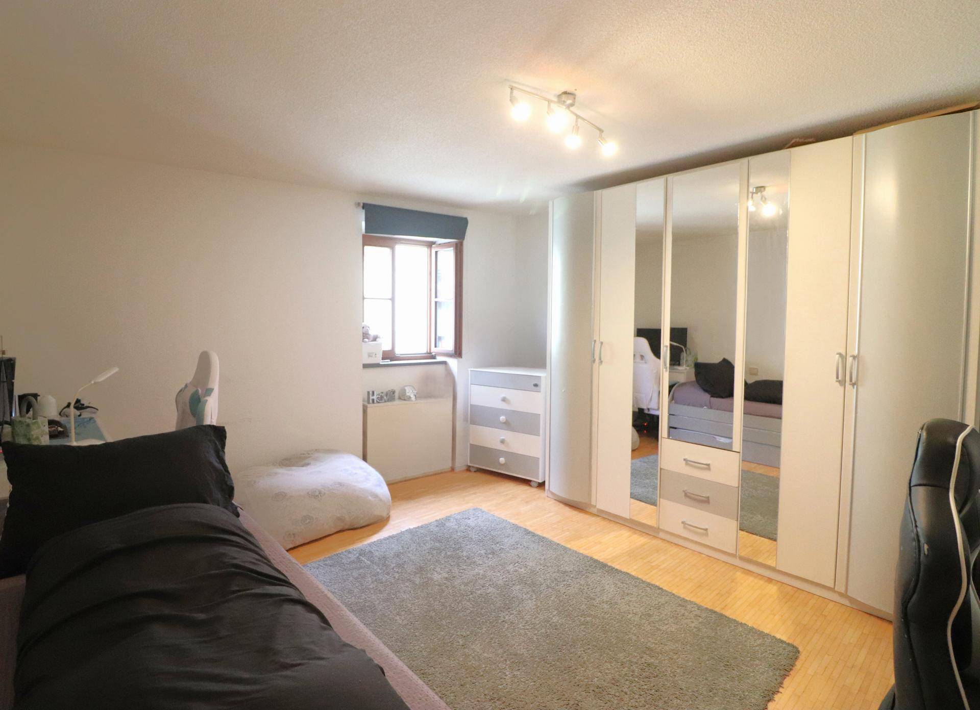Geräumiges Schlafzimmer mit großem Kleiderschrank, Holzboden und einem Fenster für Tageslicht.