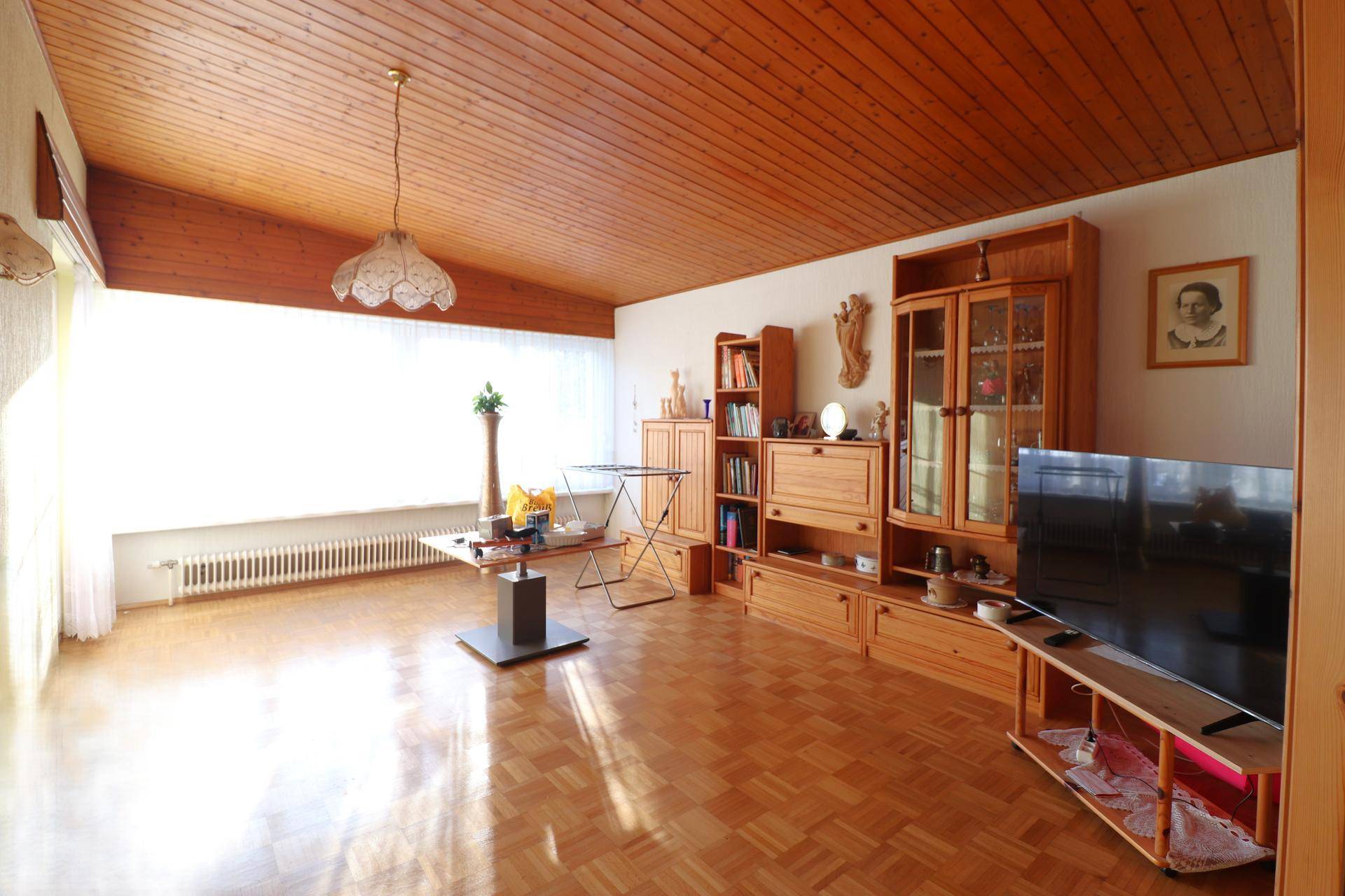 Helles Wohnzimmer mit Holzdeckenverkleidung, Parkettboden und traditionellen Holzmöbeln.