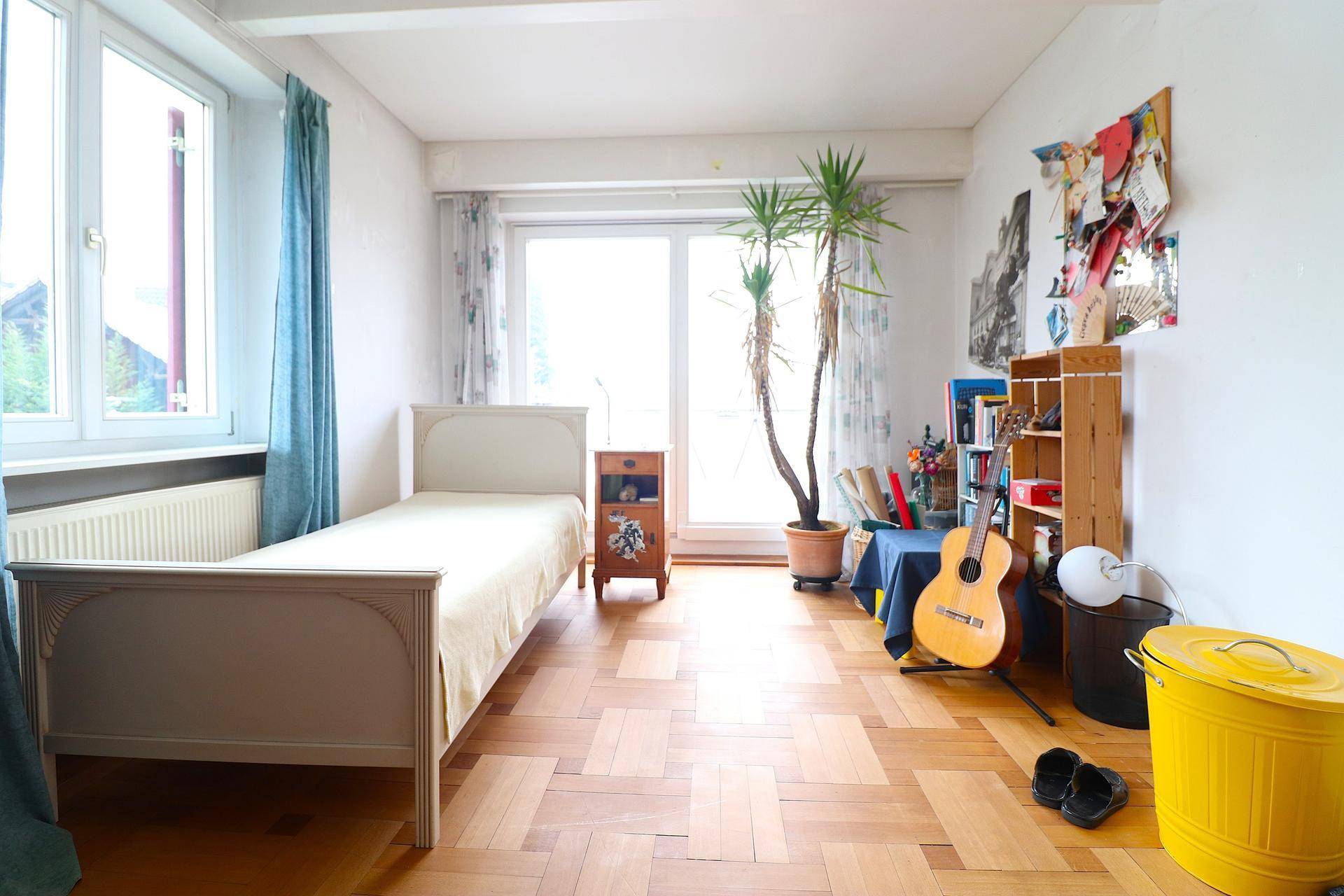 Helles Schlafzimmer mit Einzelbett, Holzboden und Zugang zu einem Außenbereich.