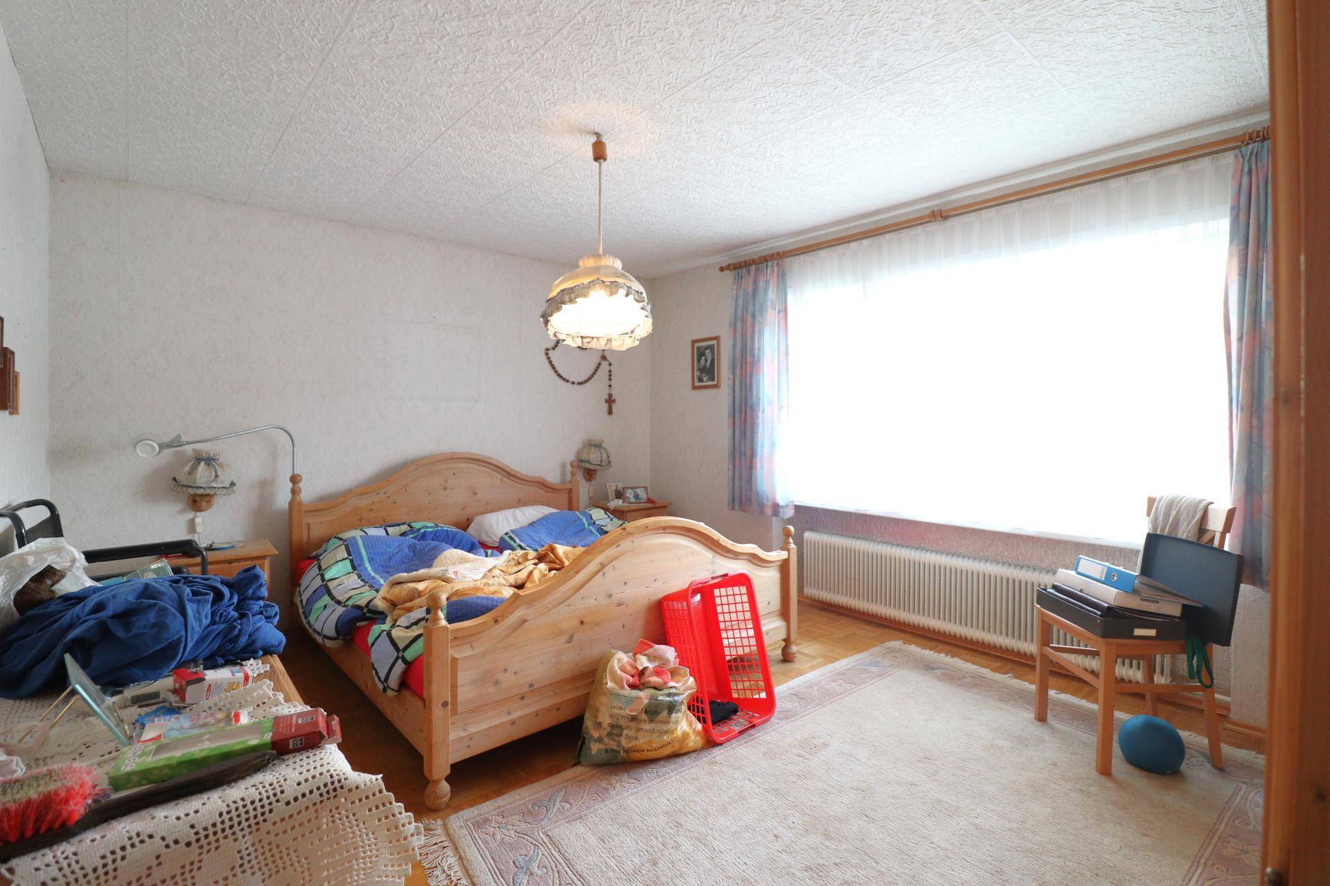 Schlafzimmer mit hellem Holzbett, Teppich und großem Fenster für viel Tageslicht.