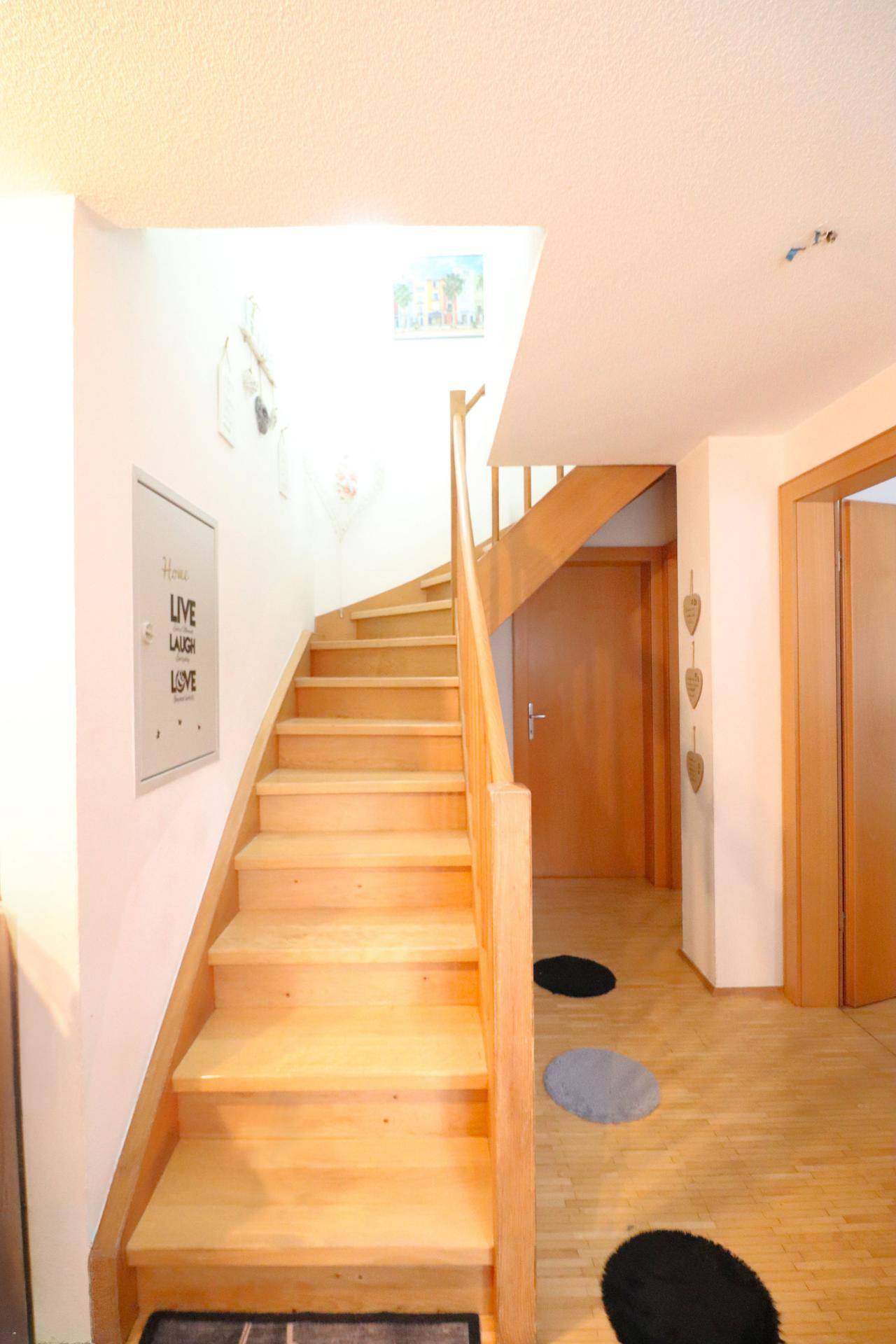 Heller Flur mit Holztreppe, die zu den oberen Etagen führt, und Holzboden.