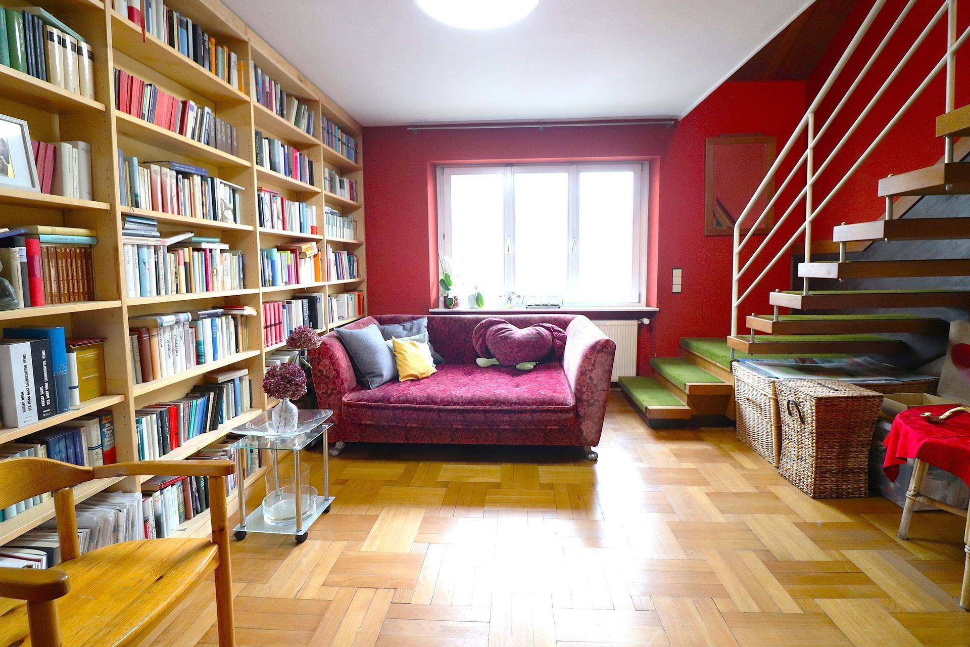 Wohnzimmer mit roter Wand, raumhohen Bücherregalen und offener Treppe.