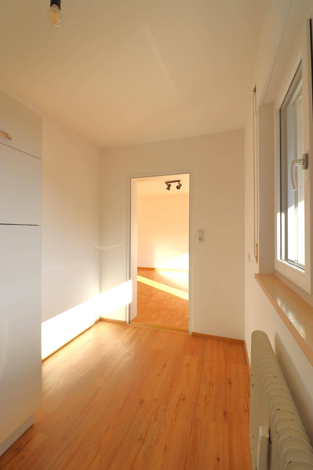 Heller Flur mit Parkettboden, der zu einem weiteren sonnigen Raum führt.