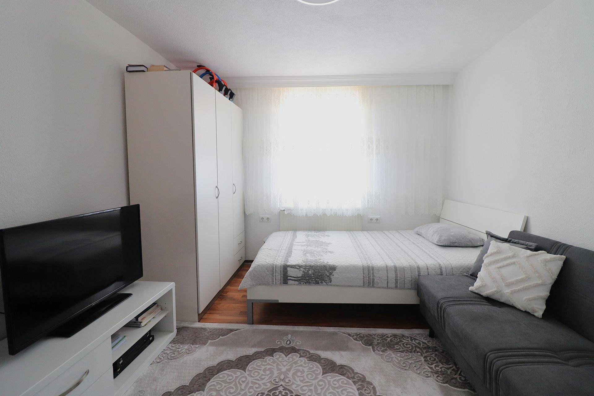 Helles Schlafzimmer mit Einzelbett, Kleiderschrank und Fernseher.