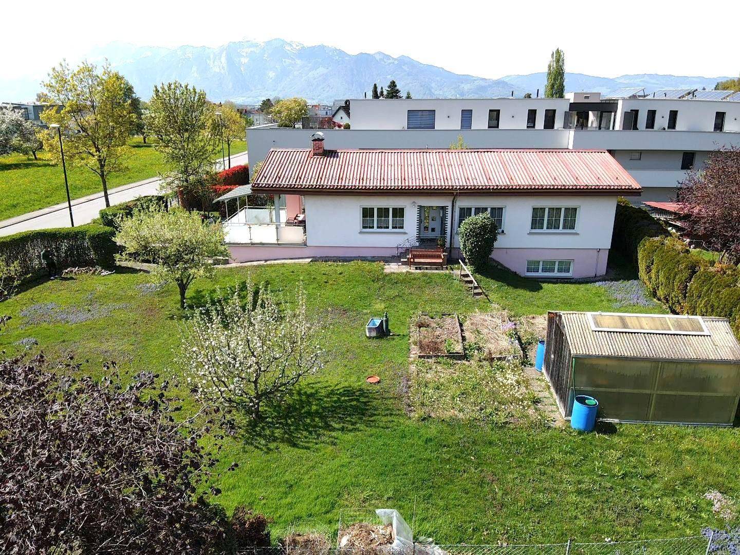 Weitläufiger Gartenbereich eines Hauses mit Gewächshaus und Blick auf die umliegende Berglandschaft.