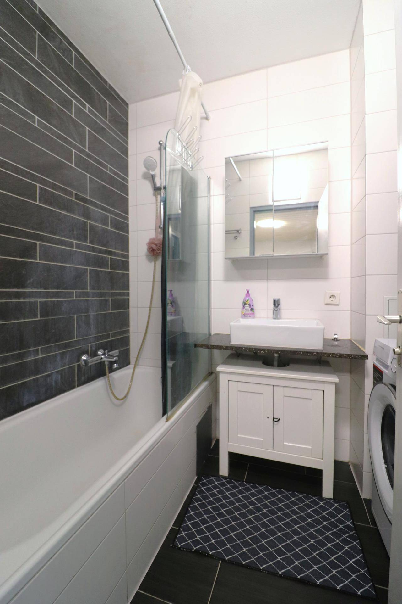 Modern gefliestes Badezimmer mit Badewanne, Dusche und Waschbecken, inklusive Waschmaschine.
