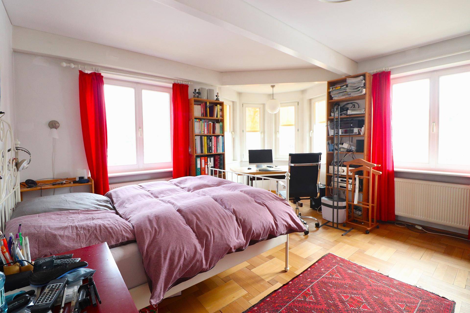 Geräumiges Schlafzimmer mit Holzboden, Schreibtischbereich und großen Fenstern.