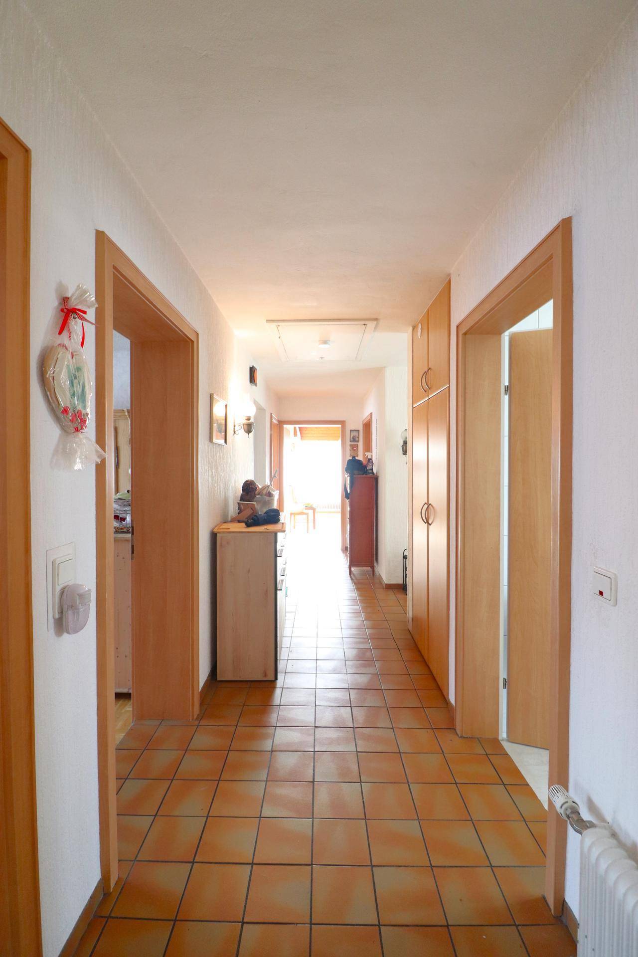 Heller Flur mit Terrakotta-Fliesenboden und praktischen Einbauschränken aus Holz.