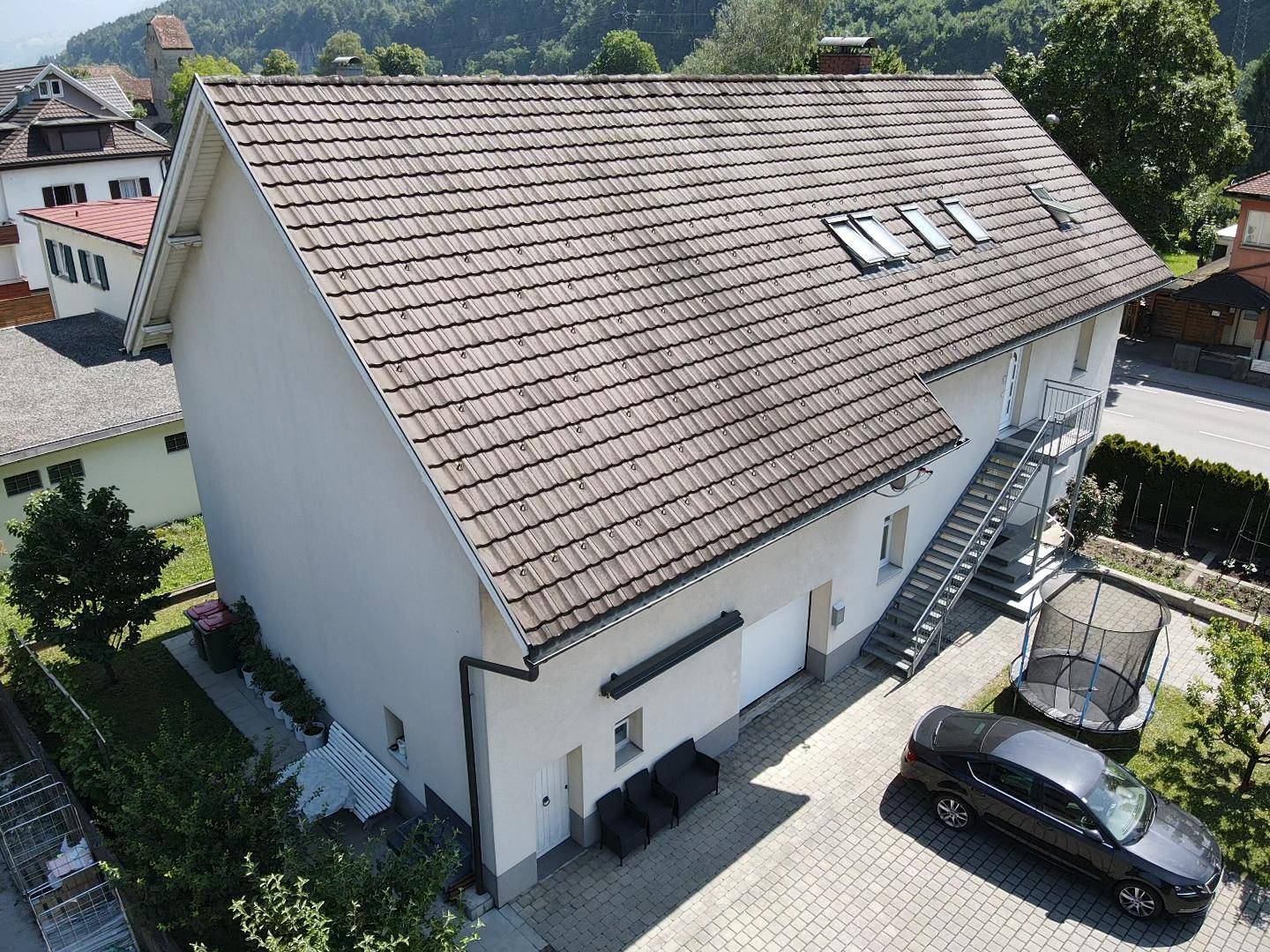 Luftaufnahme der Rückseite des Hauses mit Parkplatz, Trampolin und angrenzendem Gartenbereich.