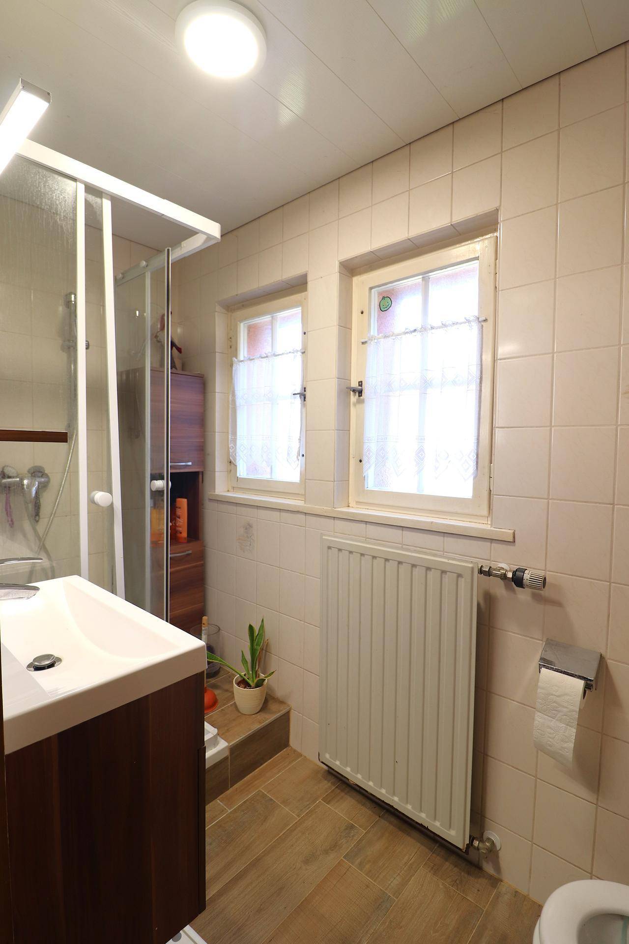 Badezimmer mit beigefarbenen Fliesen, modernem Waschtisch und Fenster für Tageslicht.