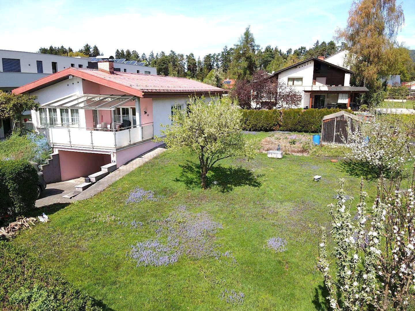 Gepflegter Garten mit Einfamilienhaus, Gewächshaus und blühenden Bäumen in ländlicher Umgebung.