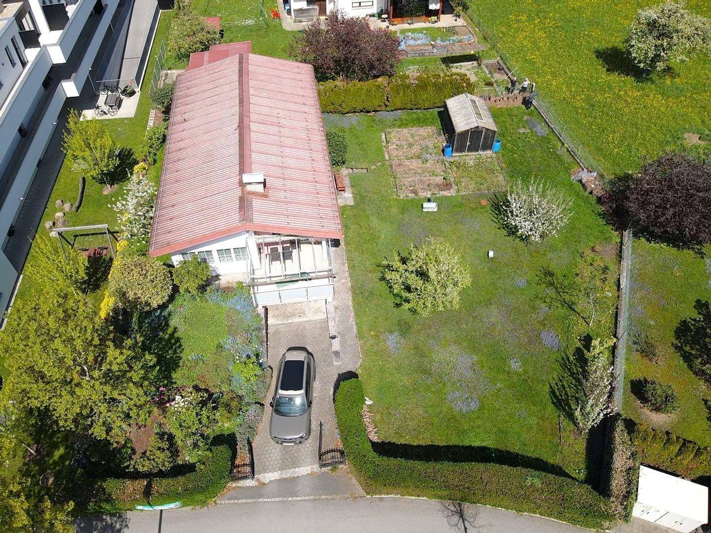 Draufsicht auf das Einfamilienhaus mit Zufahrt, Garten und angrenzenden Grünflächen.