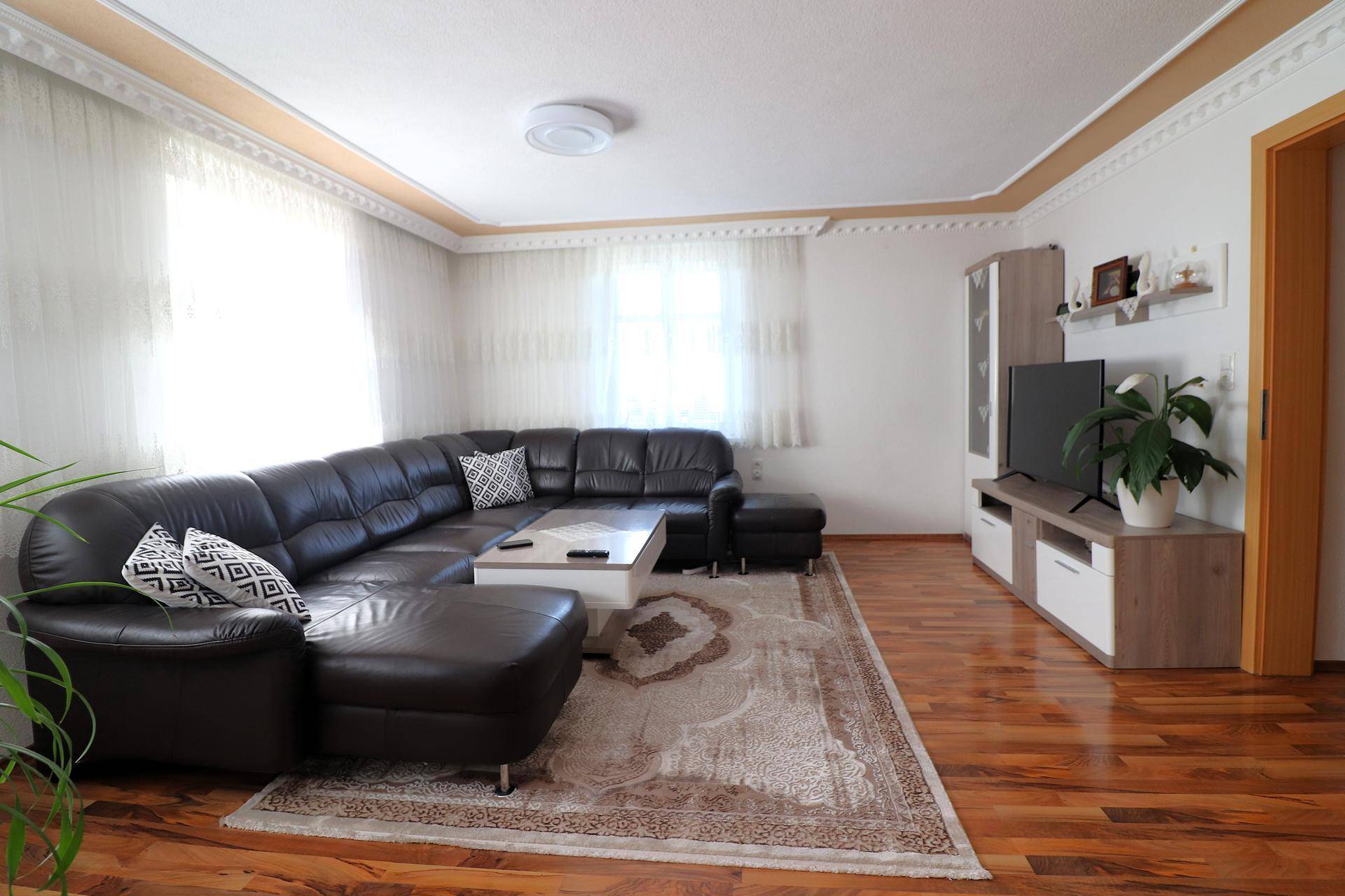 Helles Wohnzimmer mit Ledersofa, Holzboden und TV-Möbeln in modernem Stil.