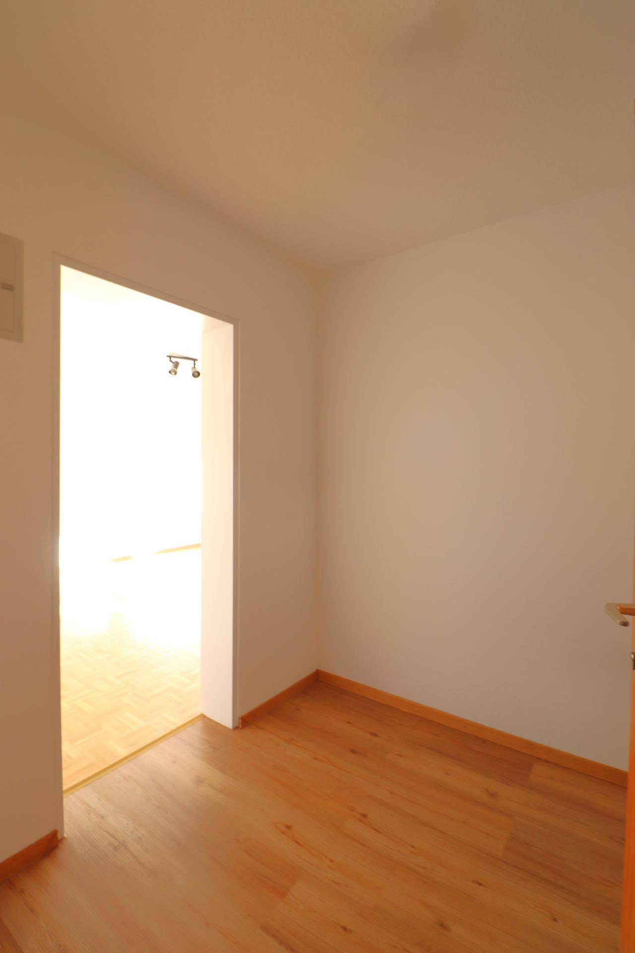 Leerer Raum mit Parkettboden und Zugang zu einem weiteren hellen Zimmer.