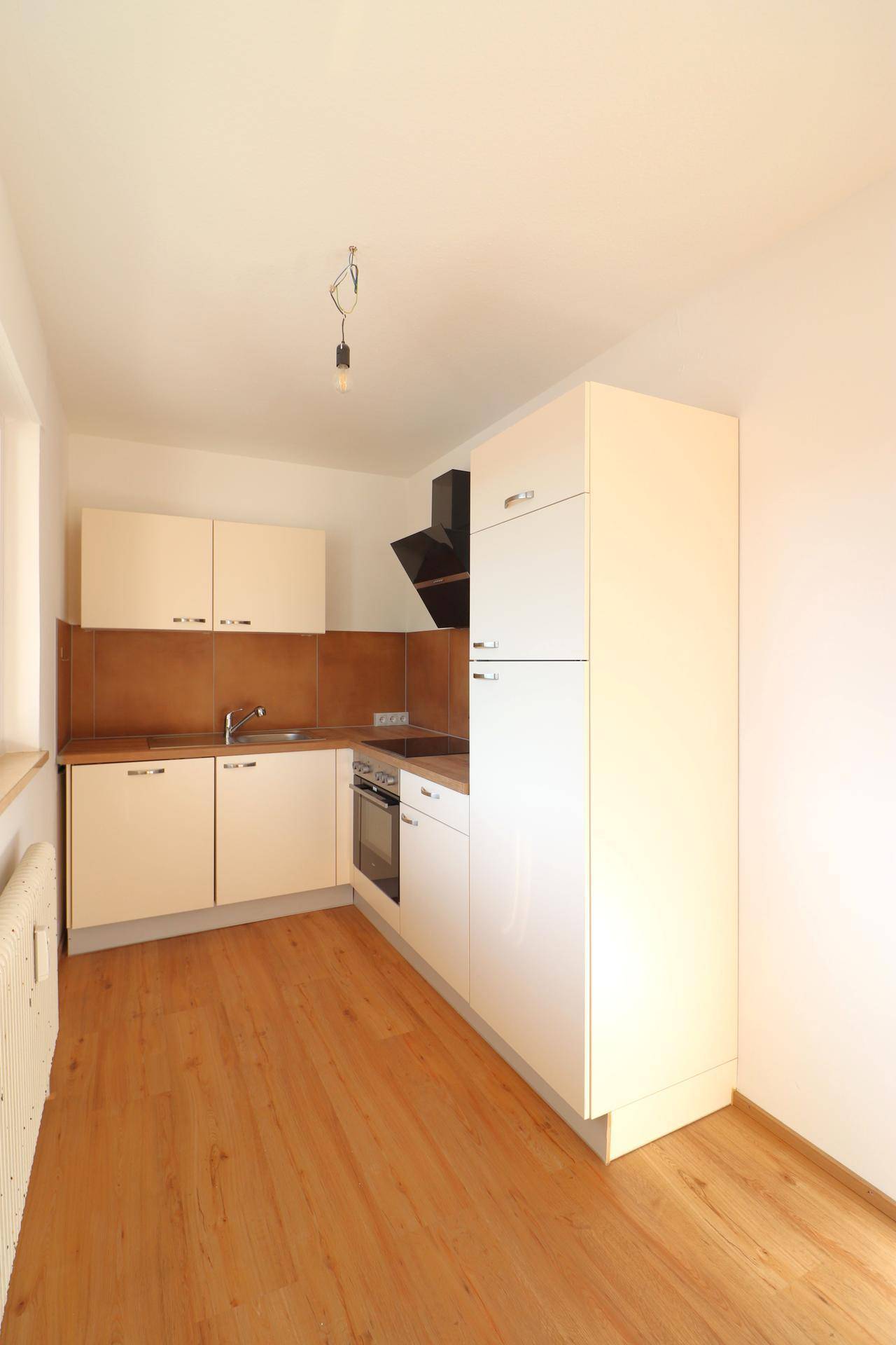 Funktionale Einbauküche mit hellen Schränken, Holzoptik-Arbeitsplatte und Parkettboden.