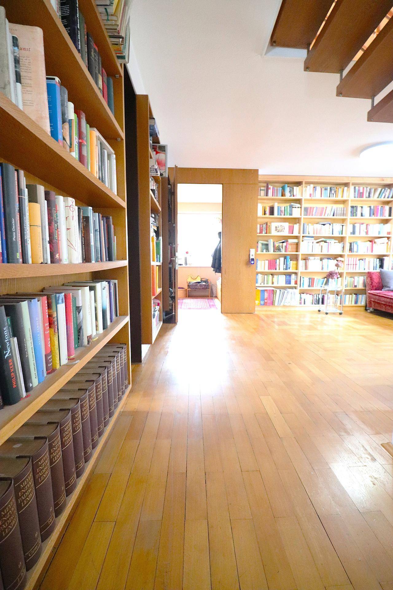Langer Raum mit umfangreichen Bücherregalen und Holzboden, der viel Stauraum bietet.