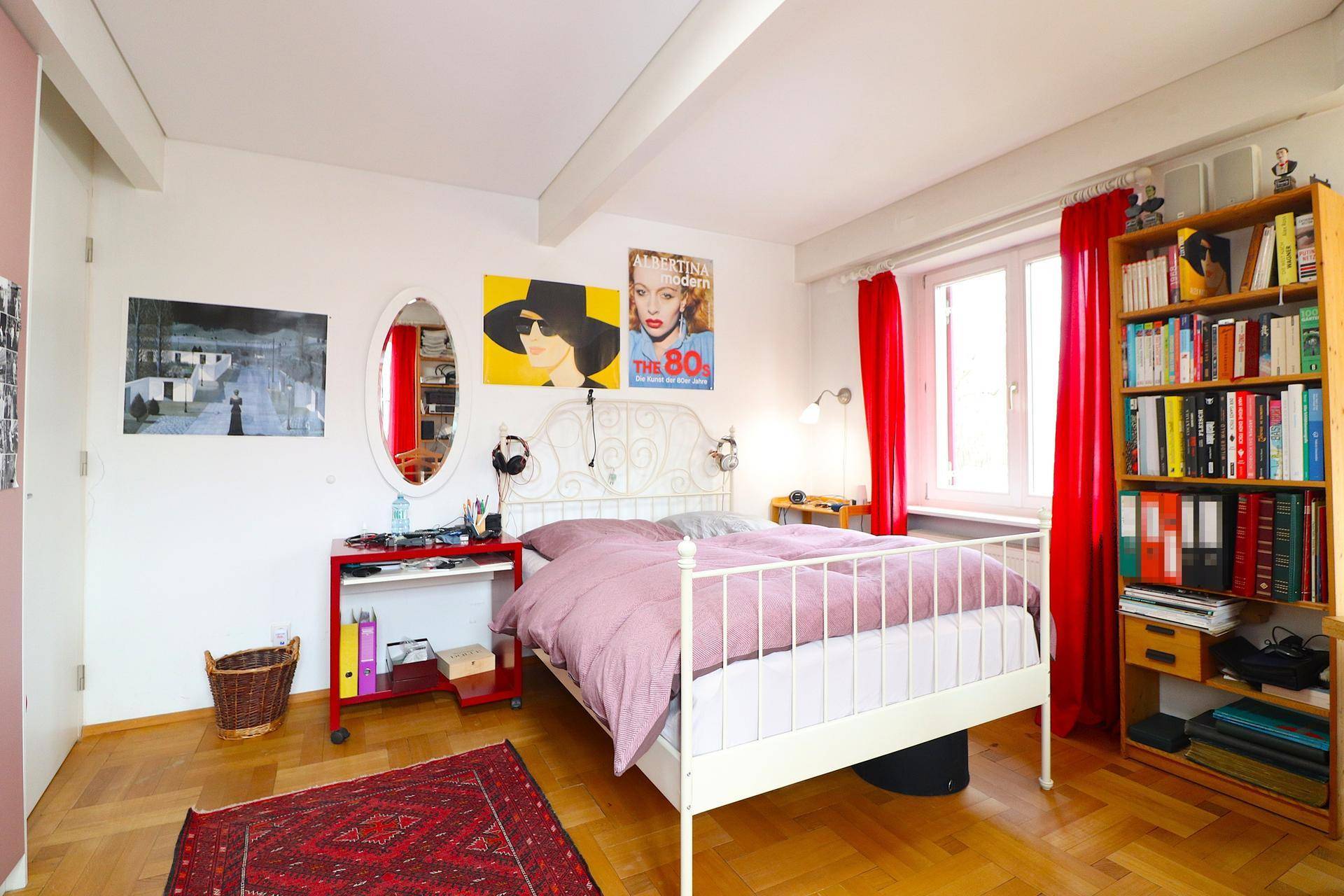 Gemütliches Schlafzimmer mit Holzboden, weißem Bettgestell und roten Vorhängen.