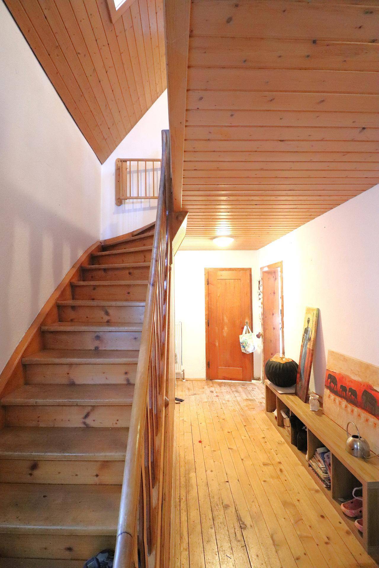 Heller Flur mit Holztreppe und Holzvertäfelung an Decke und Wänden.