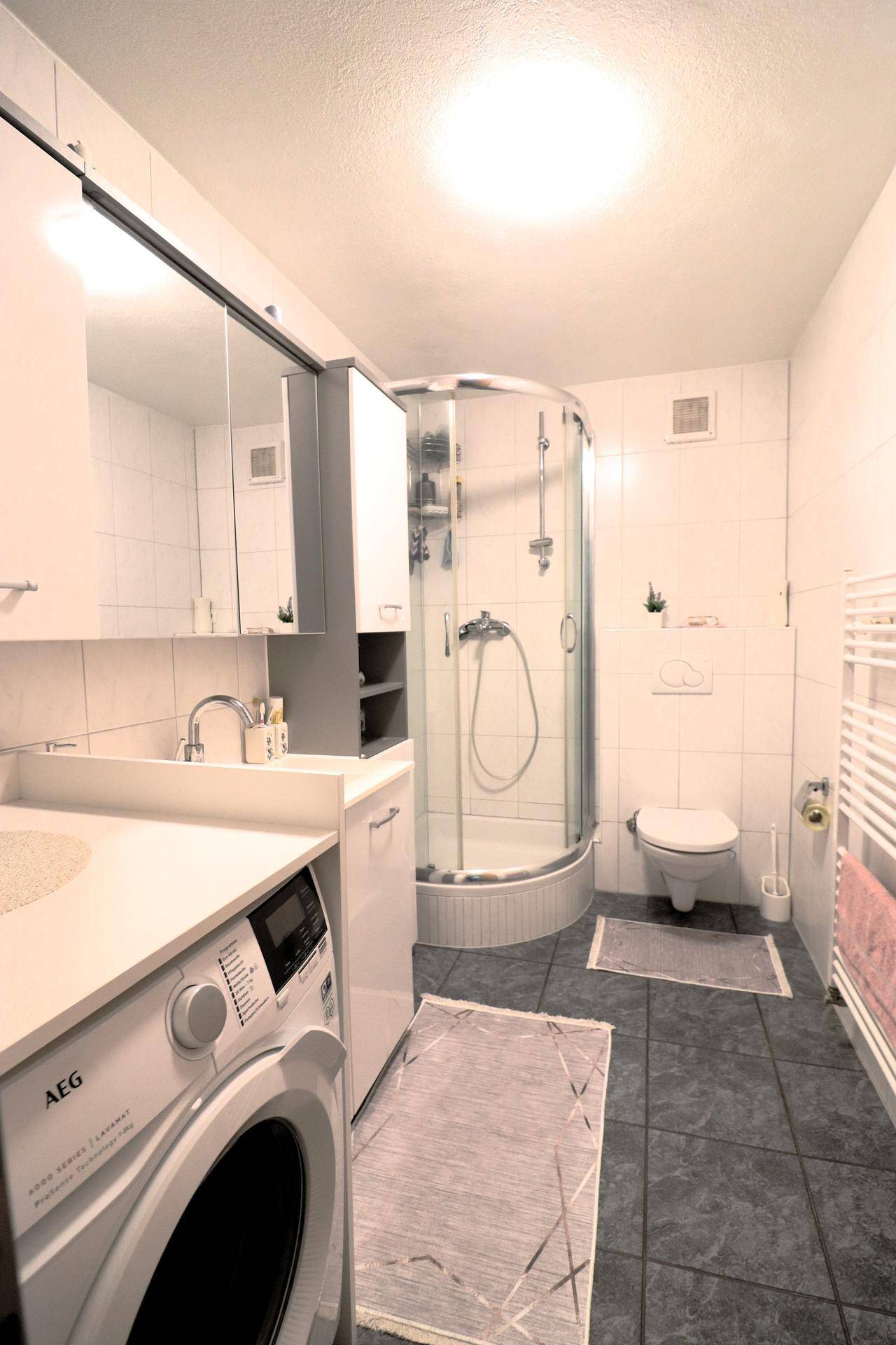 Modernes Badezimmer mit Duschkabine, WC, Waschmaschine und Spiegelschrank.